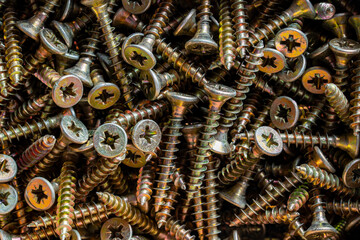 Many golden metal self tapping screws for construction work, closeup, top view. New metal fasteners self tapping screws for connecting wooden elements. Background and texture of metal screws