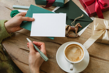 Overhead view of a mid adult woman sitting at a table with a cappuccino and a wrapped Christmas gift about to write on a blank card