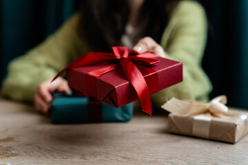 Close-up of a woman sitting at a table with wrapped Christmas gifts holding a gift box tied with a red ribbon