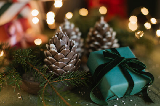 Close-up of a wrapped Christmas gift and pinecone decorations next to an illuminated Christmas tree