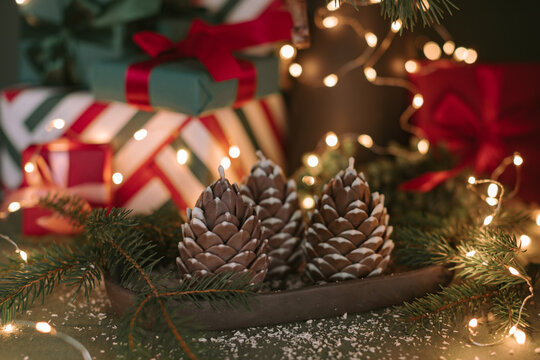 Close-up of a stack of wrapped Christmas gifts under an illuminated Christmas tree with pinecone decorations