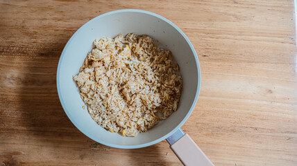 Overhead view of a light blue saucepan filled with dry oatmeal on a wooden table, ready for cooking.