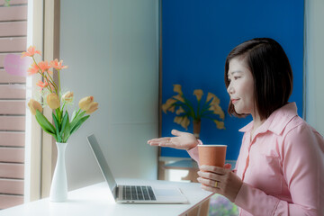 Businesswoman smiling while using laptop and talking on mobile phone at desk in office and at home or coffee shop.