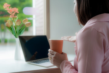 Businesswoman smiling while using laptop and talking on mobile phone at desk in office and at home or coffee shop.