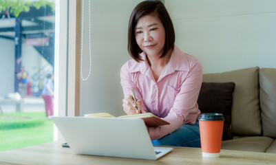 Businesswoman smiling while using laptop and talking on mobile phone at desk in office and at home or coffee shop.