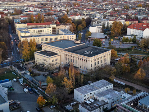 Aerial view of the imposing Berghain nightclub, its concrete facade a stark contrast to the autumn trees, under a soft, diffused light, Berlin, Berlin, Germany.