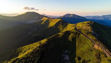 An aerial view captures a winding road traversing a lush green mountain range, bathed in the warm glow of sunset.