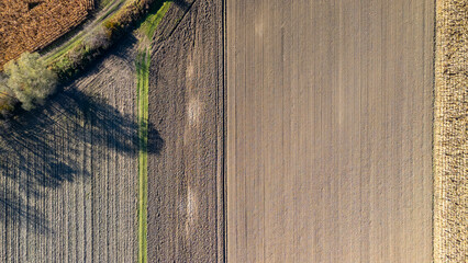 Aerial view of agricultural fields showcasing distinct patterns and textures. The photograph captures the rich brown soil and green pathways. Ideal for environmental themes.