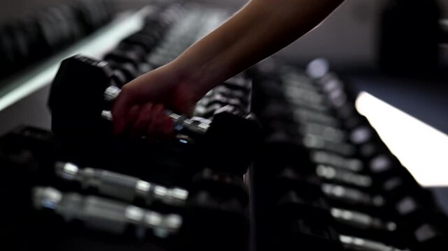 A woman in a modern gym returning dumbbells to the rack after an intense workout session. The scene shows proper gym etiquette, organized equipment, and a focused post training atmosphere.