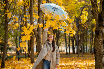 Conceptual portrait of woman in autumn park lifting umbrella with falling yellow maple leaves