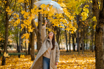 Conceptual portrait of woman in autumn park lifting umbrella with falling yellow maple leaves