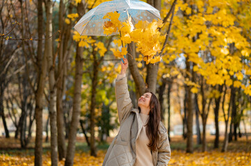 Conceptual portrait of woman in autumn park lifting umbrella with falling yellow maple leaves