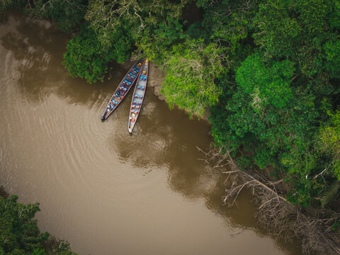 Aerial view of two canoes resting on the murky riverbank, embraced by the lush, vibrant green canopy of the Amazon Rainforest, Tipishca, Sucumbios, Ecuador. - Powered by Adobe