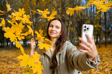 Autumn selfie concept – young woman smiling among yellow maple leaves