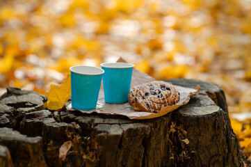 Autumn picnic concept - cups and pastries on old tree stump among colorful leaves