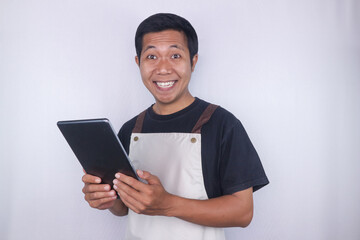 Smiling young Asian man barista barman employee wearing apron hold digital tablet isolated white