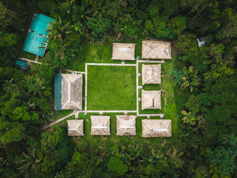 Aerial view of a symmetrical arrangement of quaint buildings with weathered roofs surrounding a vibrant green courtyard, nestled deep within the lush Amazon rainforest, Tipishca, Sucumbios, Ecuador.