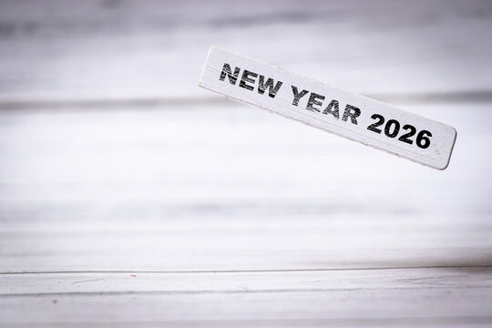 Handwritten text reading NEW YEAR 2026 on a white wooden table evokes feelings of celebration and new beginnings, perfect for planners and event organizers.