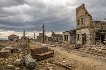 Desolate landscape featuring ruined buildings, weathered sofa, and barren road under cloudy sky, evoking sense of abandonment and decay
