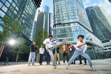 A group of sporty people of different ages in business outfits training capoeira in a big city