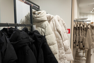 Black and white winter coats are neatly arranged on racks inside a retail clothing store. The coats are displayed in a well-lit, modern shopping environment.