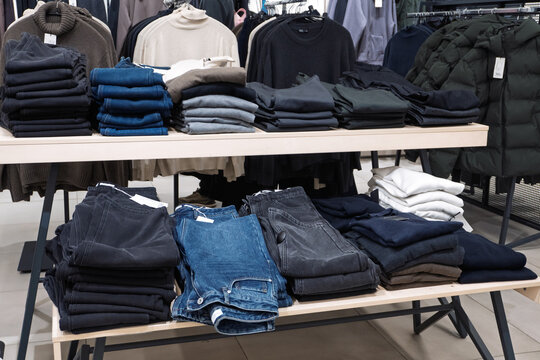 A retail store display features neatly folded jeans and sweaters arranged on a two-tier wooden table. Various shades of denim and knitwear are organized for customer browsing.