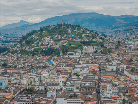 Aerial view of the city stretching towards the iconic Panecillo hill crowned with the Virgin of El Panecillo statue under a cloudy sky, Quito, Ecuador.