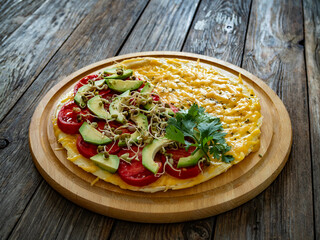 Italian piada - piadina with tomatoes, avocado, bean sprouts, scrambled eggs and cheddar cheese on wooden table	