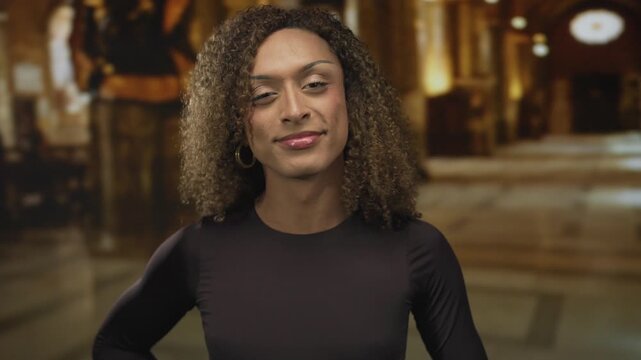 Woman wearing black top points finger to camera in church nave under warm lighting; confidence empowerment.