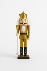 Golden Christmas nutcracker figurine standing on a white background. Classic festive decor with crown, staff and glitter details. Perfect for holiday themes, winter interiors and seasonal design.