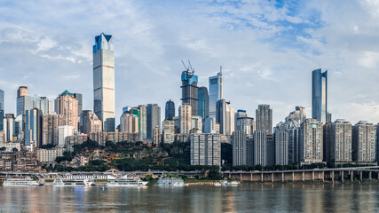 Obraz premium Modern city skyline and waterfront architecture with tour boats on the river under a blue sky in Chongqing.