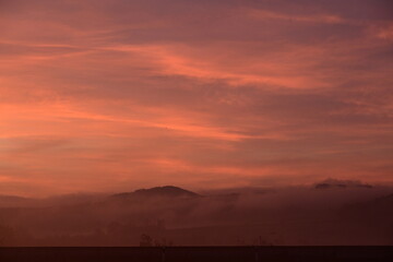 Bewaldeter Hügel ragt aus dem Nebel bei Sonnenaufgang