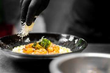 Chef adding shredded cheese to a delicious-looking shrimp and broccoli dish on rice in a black bowl.