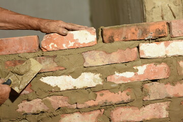 One hand holds a freshly laid brick while the other removes excess clay with a trowel.