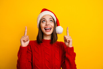 Funny festive moment as a young pretty woman in a red sweater and santa hat points up with joy