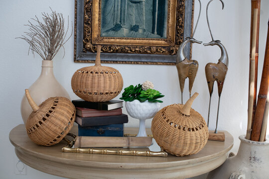 Autumn tabletop vignette with wicker pumpkins, vintage books, and white compote planter, natural light, thanksgiving and fall decor