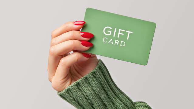 female hand with red polished nails and green sweater holding a green gift card, perfect for holiday shopping or presents