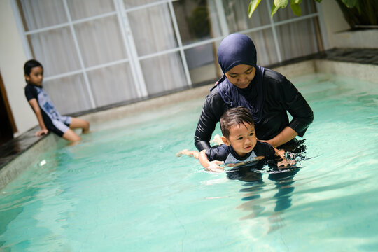 A mother guides her young child while practicing swimming in a shallow outdoor pool.