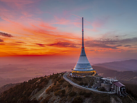Aerial view of the iconic Jestěd tower piercing the vibrant sunset sky, its unique silhouette a beacon against the Czech landscape, Liberec, Liberecky kraj, Czechia.