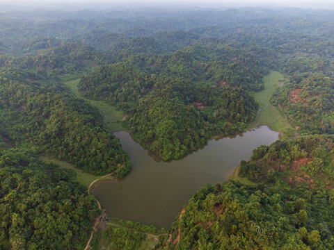 Aerial view of a placid lake nestled amidst a vibrant green forest, the water reflecting the sky, a serene landscape, Sherpur, Mymensingh Division, Bangladesh.