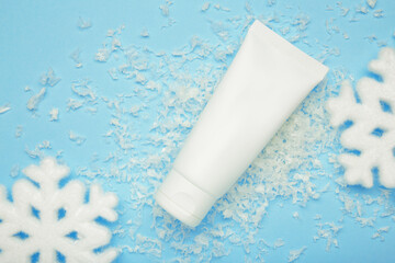 Winter skin care concept. Cosmetic moisturizer cream and snowflakes on blue background.