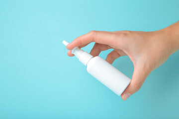 Hand holds a bottle of nasal drops on blue background.