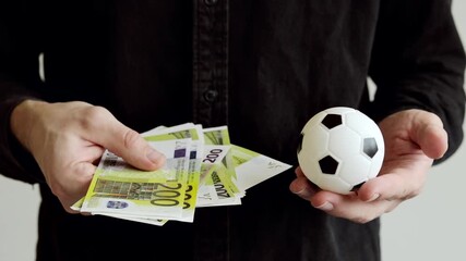 Euro banknotes and small soccer ball in hand. Corruption in football. - Powered by Adobe