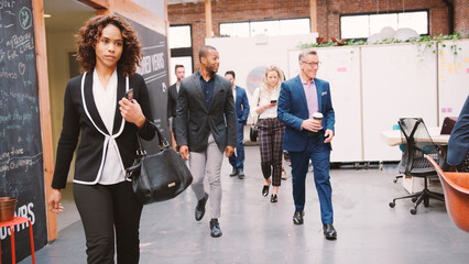 Businesspeople Arriving For Work In Busy Modern Open Plan Office