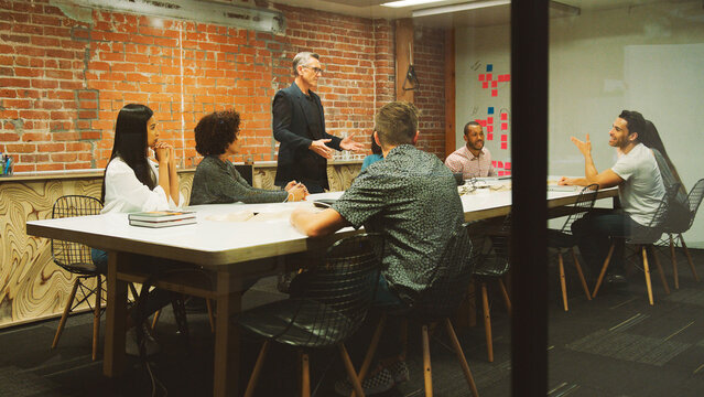 Mature Businessman Standing And Leading Office Meeting Around Table