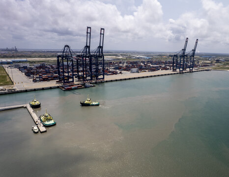 Aerial view of towering cranes overlooking the docks where tugboats sit idle, a stark contrast against the murky water, Lekki, Nigeria.