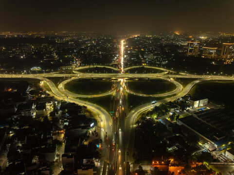 Aerial view of the illuminated cloverleaf interchange, its swirling ramps glowing against the dark canvas of the city night, a modern marvel of urban design, Gurugram, Haryana, India.