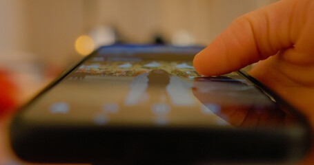 Smartphone user navigating digital content through smooth finger scrolling, revealing blurred holiday background with soft bokeh lighting