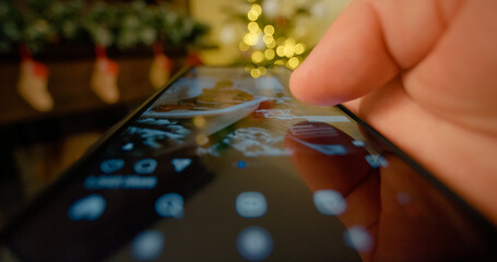 Close up of finger scrolling through social media feed on a smartphone screen against the backdrop of Christmas decorations