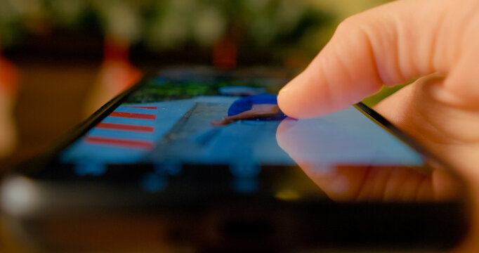 Smartphone finger scrolling touchscreen with soft Christmas lights glowing in blurred background, showcasing digital connection during festive evening